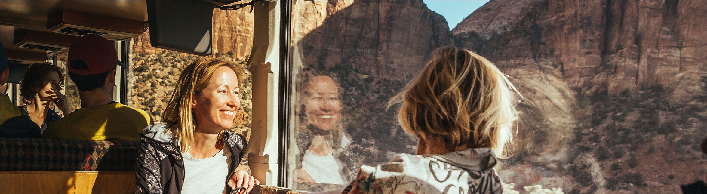 Reflections of a woman smiling in the windows of a Green Tortoise adventure coach.