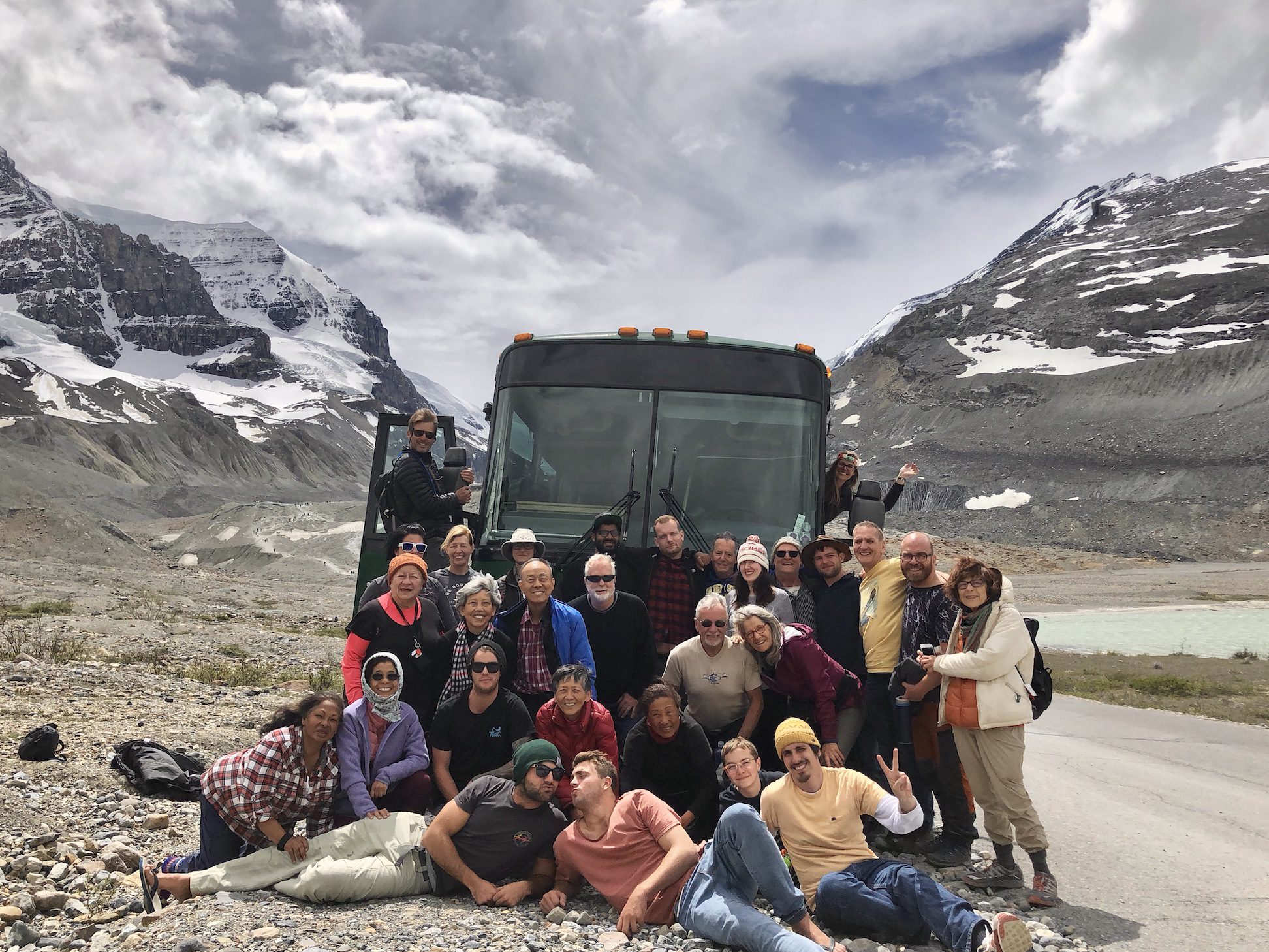 Alaska group poses in front of their adventure coach at the face of a glacier.