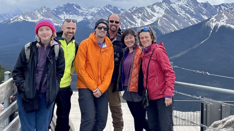 A group of Green Tortoise travelers pose in front of snowy peaks on a camping adventure in Banff National Park in the Canadian Rockies