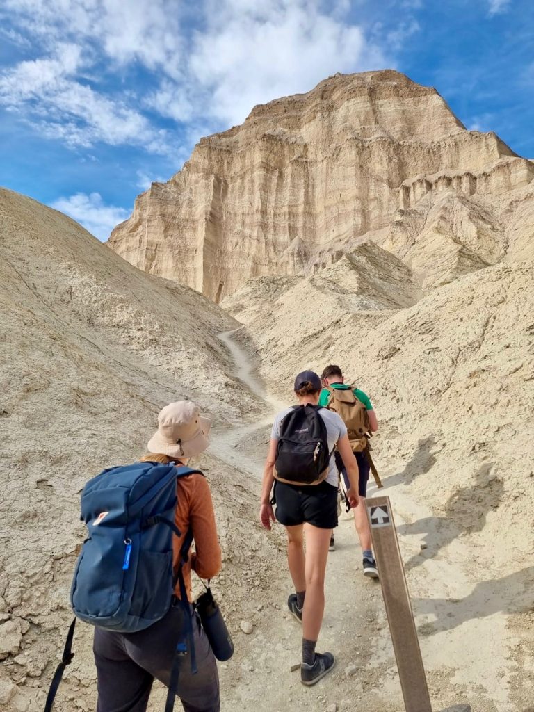 Three people are hiking with backpacks up a trail in Death Valley National Park.
