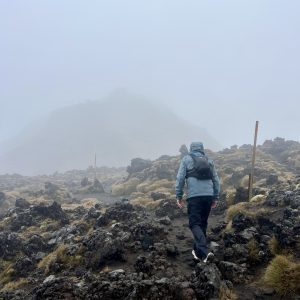 A man hikes on rocky terrain in a volcanic landscape