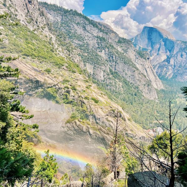 A rainbow in the foreground of a photo of Half Dome at Yosemite National Park