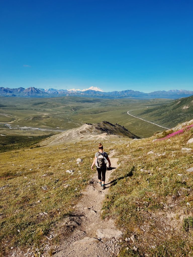 Woman hiking on a trail with the view of Denali on an Alaska camping adventure