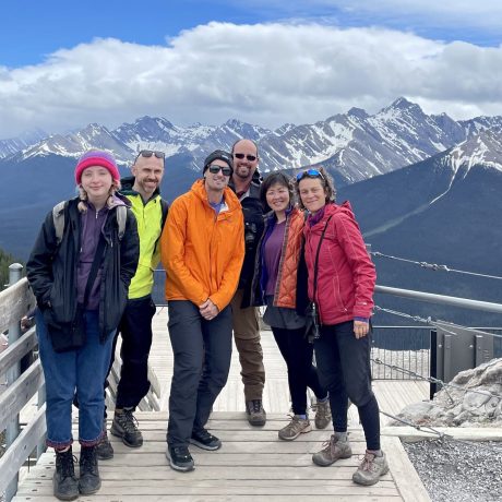 A group of Green Tortoise travelers pose in front of snowy peaks on a camping adventure in Banff National Park in the Canadian Rockies