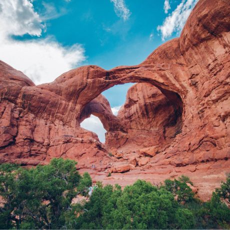 A red rock arch dramatically rises into the sky.